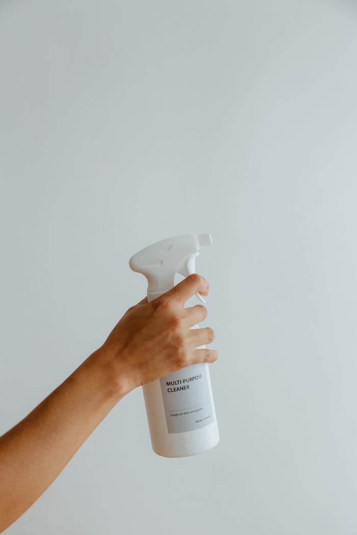 Close-up of a hand holding a white multipurpose cleaner spray bottle against a minimalistic background.